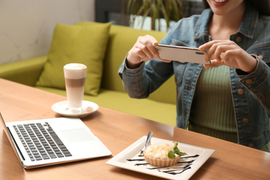 Photo of Blogger taking picture of cake at wooden table in cafe, closeup