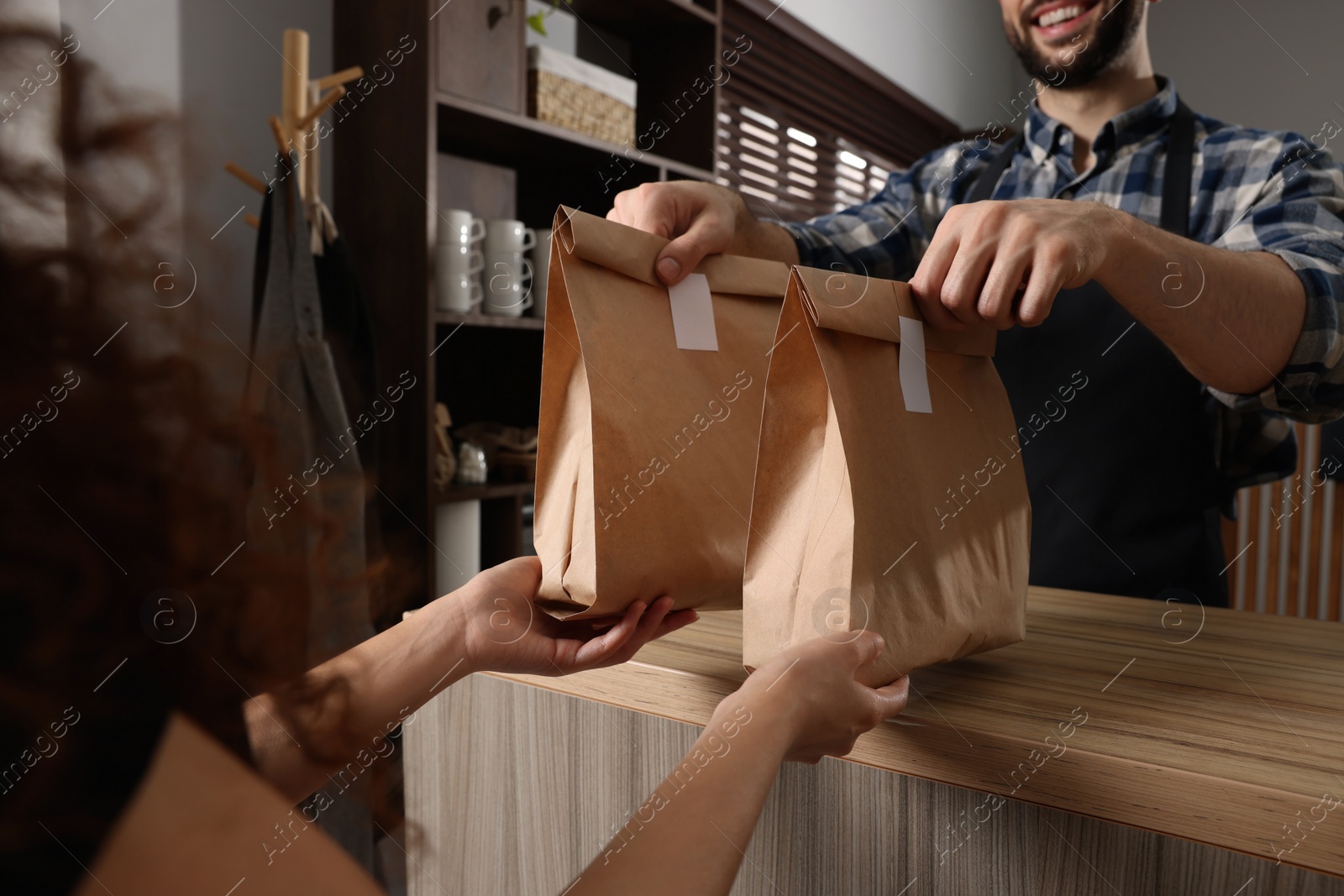 Photo of Worker giving paper bags to customer in cafe, closeup