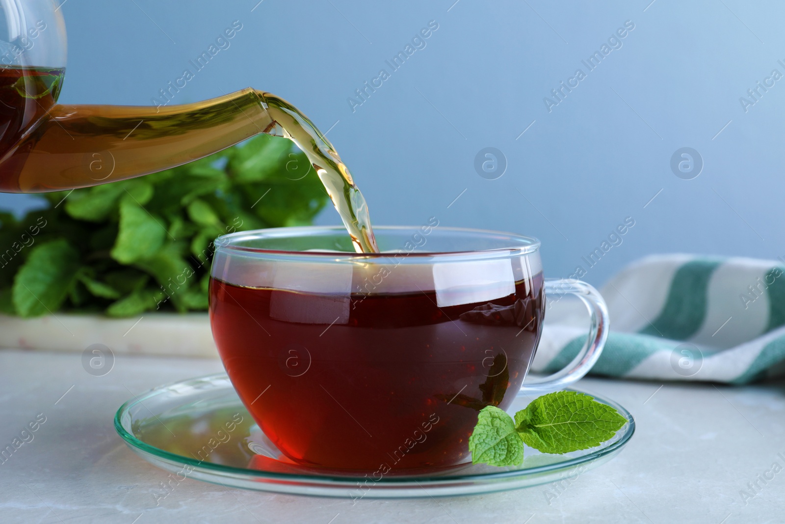 Photo of Pouring fresh mint tea into cup on light table, closeup