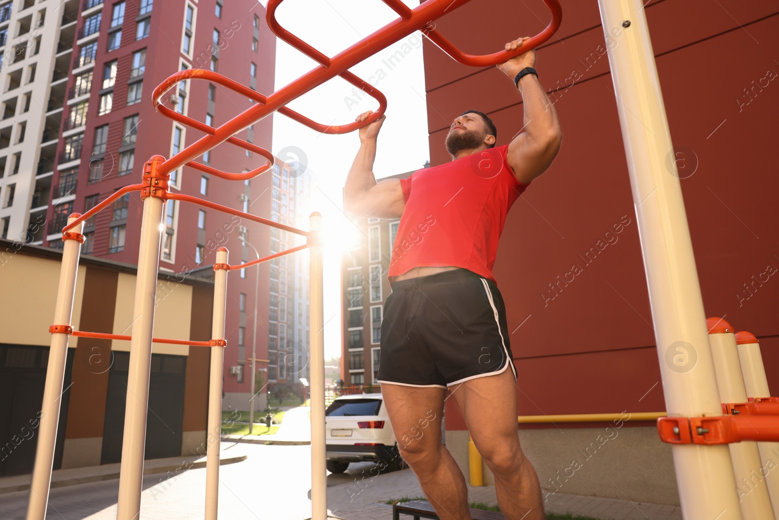 Photo of Man training on horizontal bars at outdoor gym on sunny day, low angle view