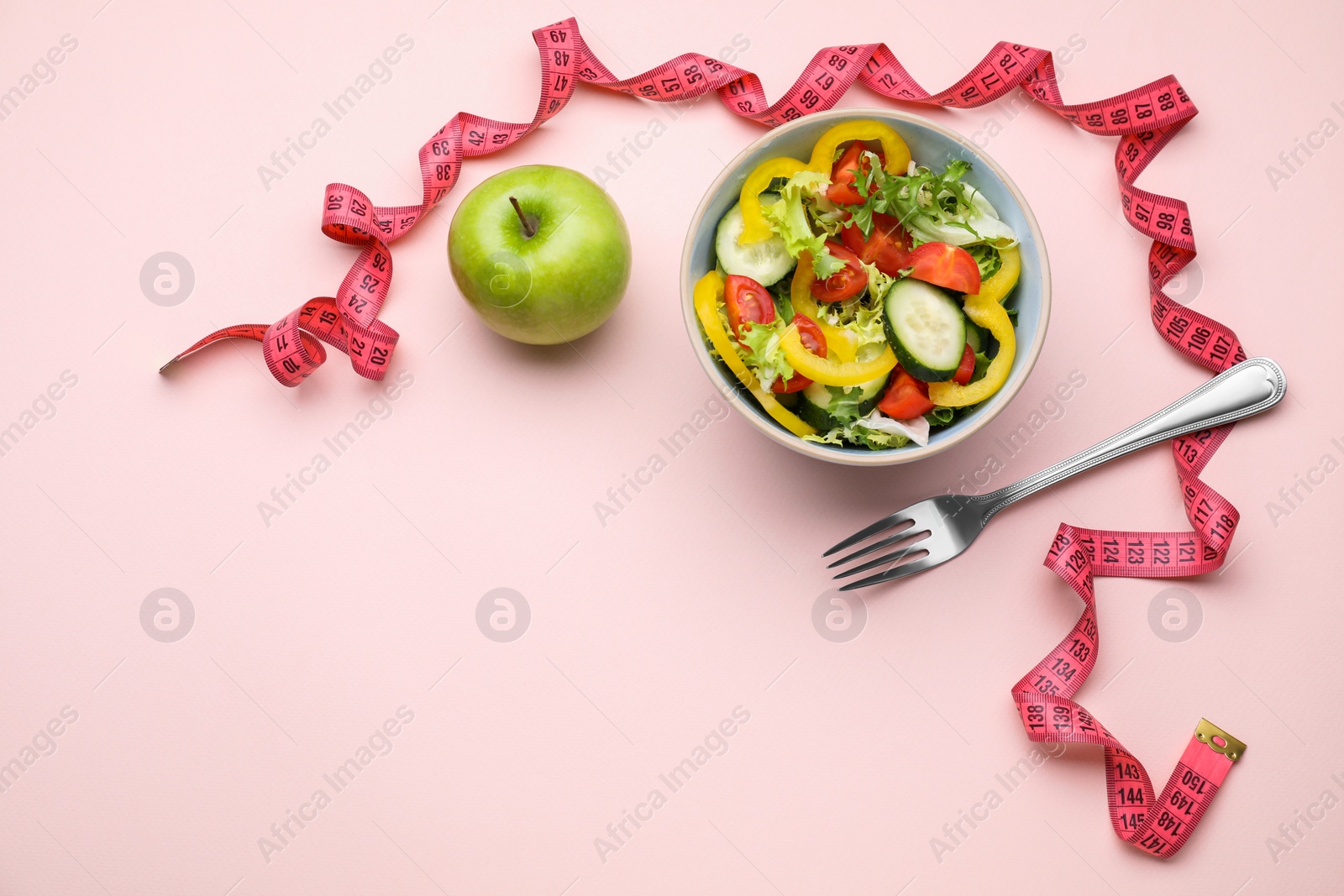 Photo of Measuring tape, salad, apple and fork on pink background, flat lay. Space for text