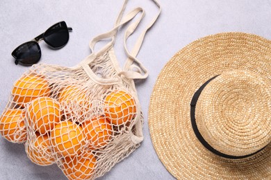 Photo of String bag with oranges, sunglasses and straw hat on grey table, top view