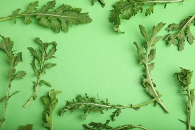 Frame of fresh arugula on green background, flat lay. Space for text