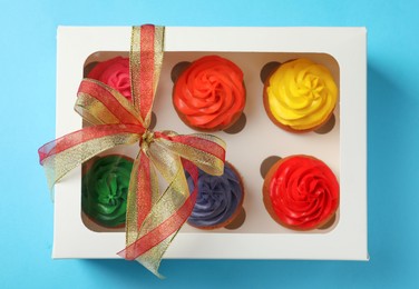 Box with delicious colorful cupcakes on light blue background, top view
