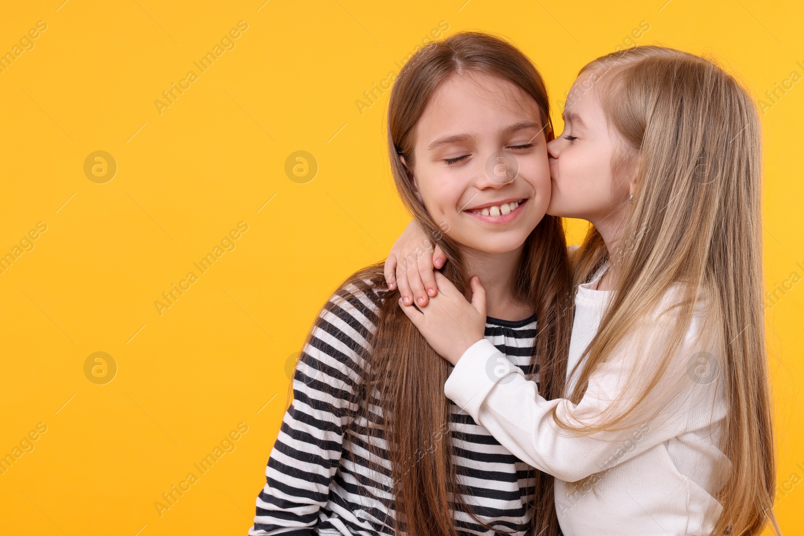 Photo of Portrait of cute little sisters on orange background, space for text