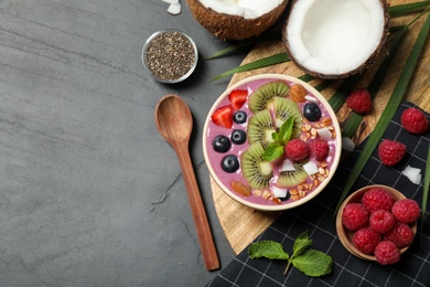 Photo of Delicious acai smoothie with granola and fruits served on black table, flat lay