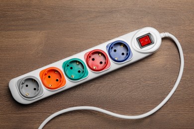 Photo of Power strip with extension cord on wooden floor, top view. Electrician's equipment