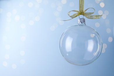 Photo of Transparent glass Christmas ball against light background with festive lights. Space for text