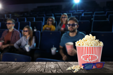 Popcorn, 3D glasses on table and young people in cinema hall, space for text 