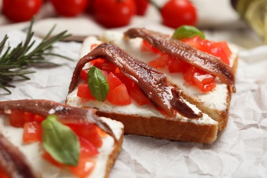 Delicious sandwiches with cream cheese, anchovies, tomatoes and basil on parchment paper, closeup