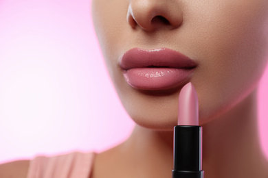 Woman with glossy lipstick on pink background, closeup