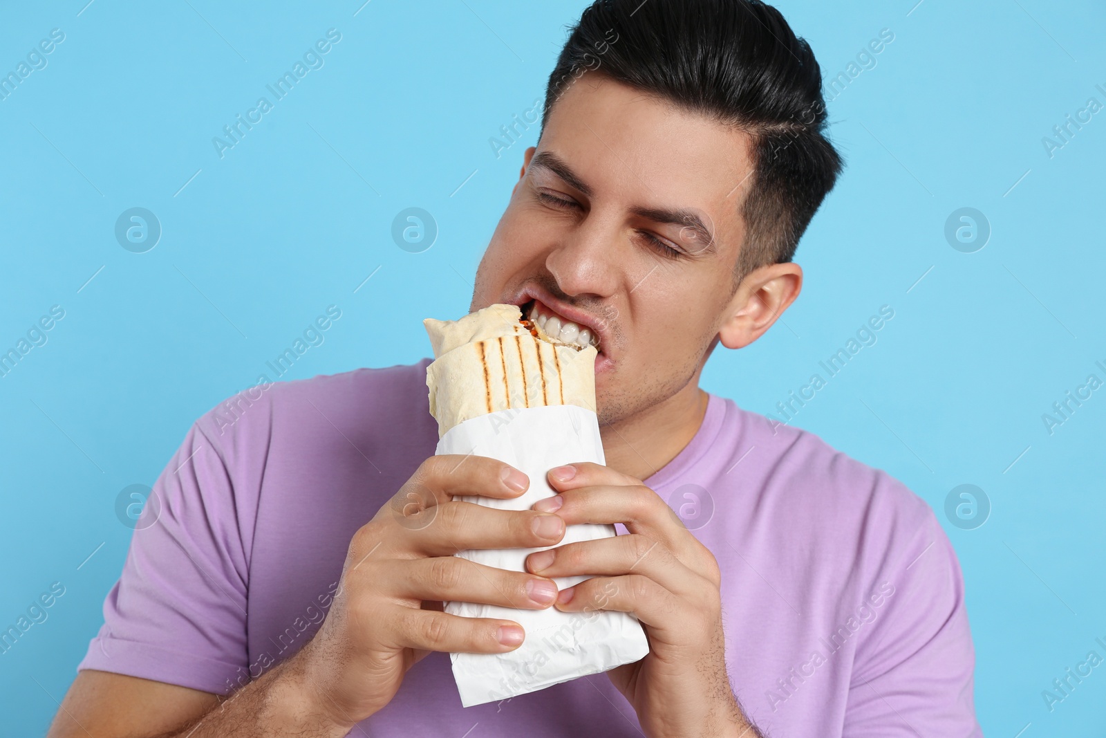 Photo of Man eating delicious shawarma on turquoise background