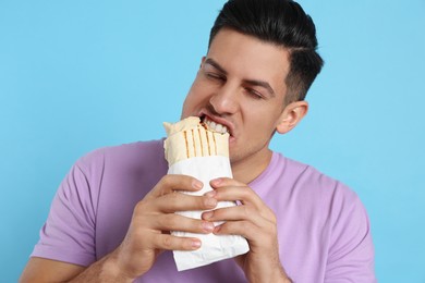 Man eating delicious shawarma on turquoise background