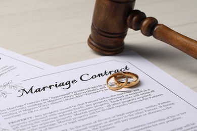 Photo of Marriage contracts, gold rings and gavel on light wooden table, closeup