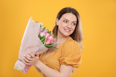 Photo of Happy young woman with bouquet of beautiful tulips on yellow background