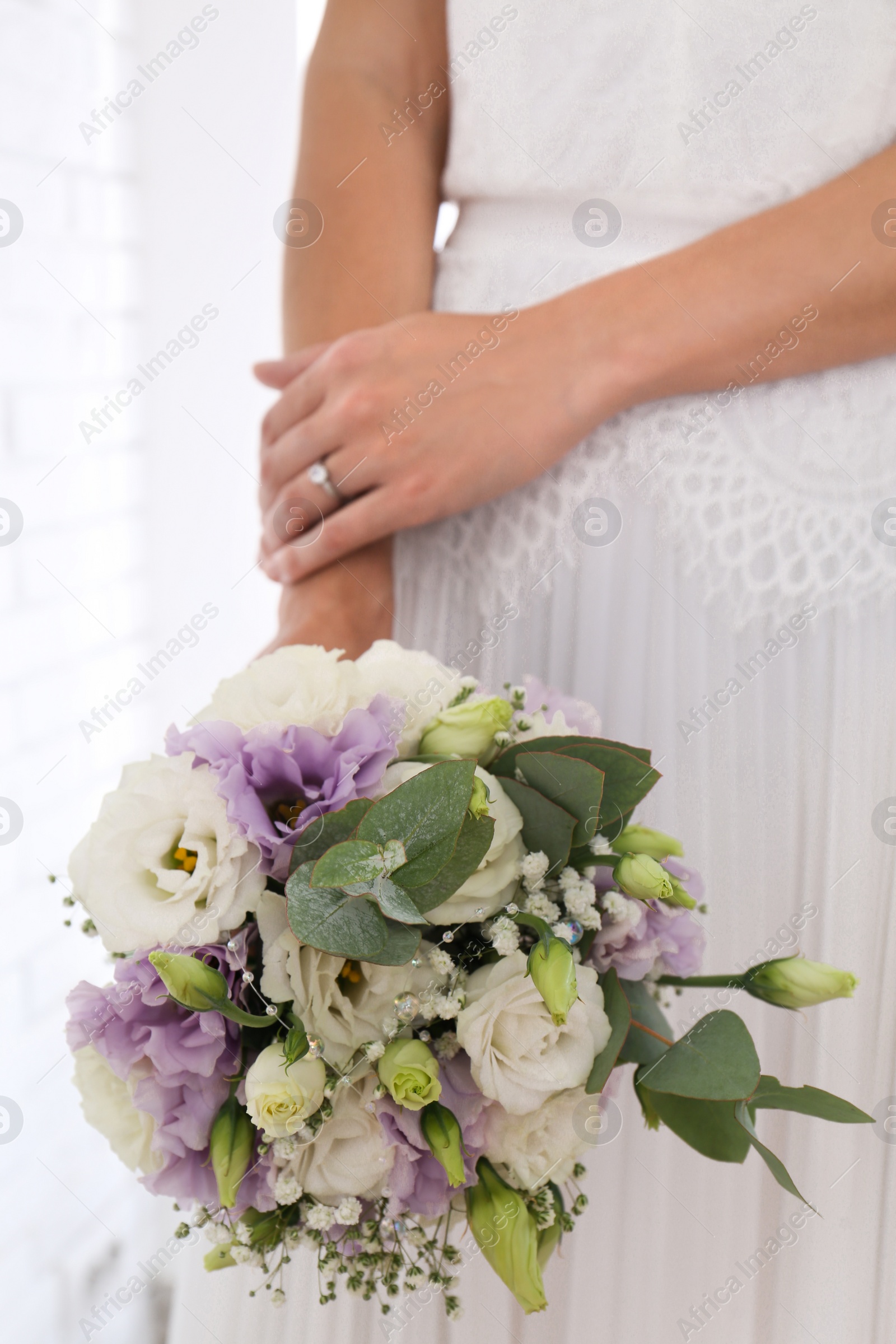 Photo of Bride holding beautiful bouquet with Eustoma flowers indoors, closeup