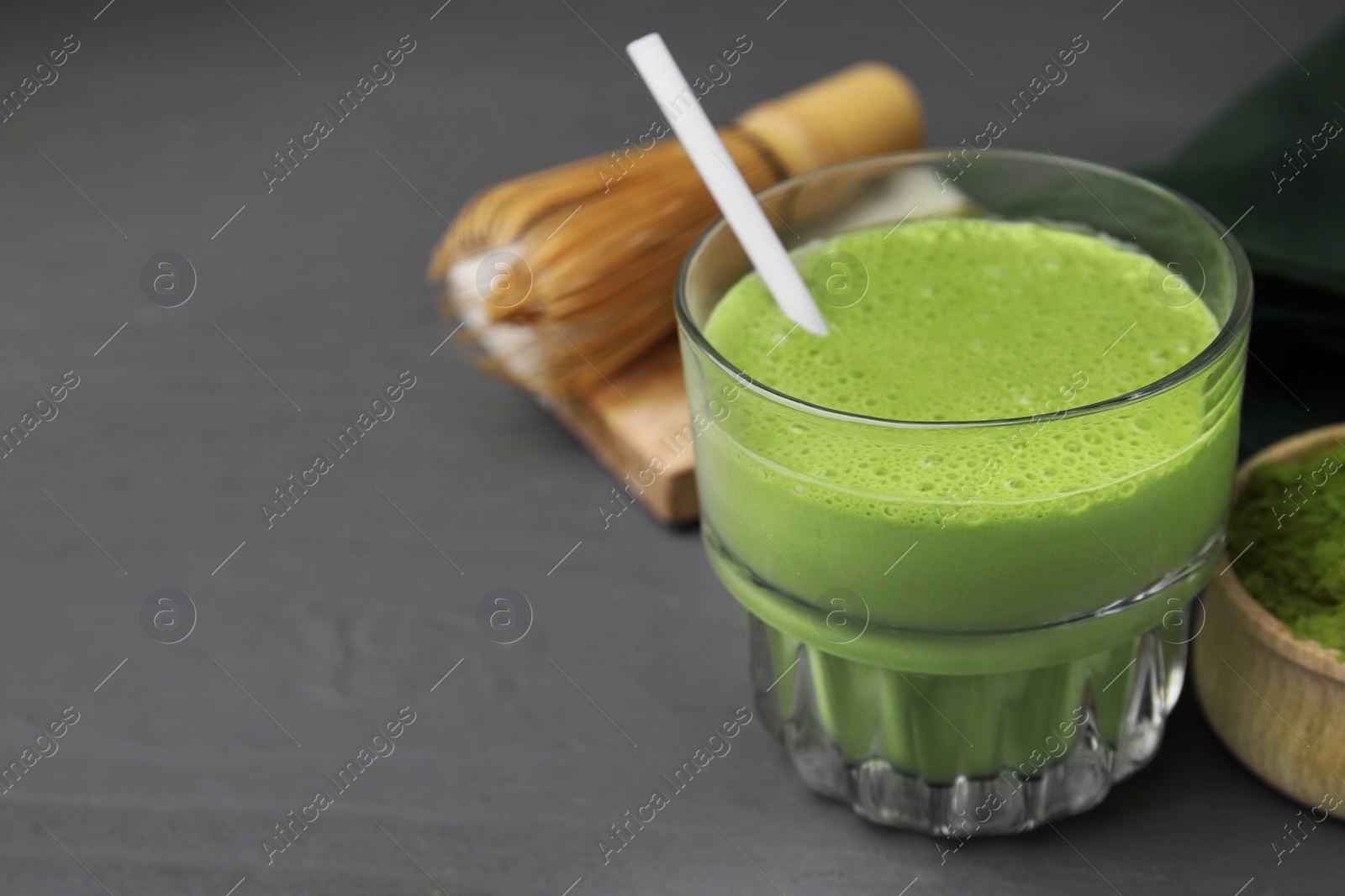 Photo of Glass of tasty matcha smoothie with straw on grey wooden table, closeup. Space for text