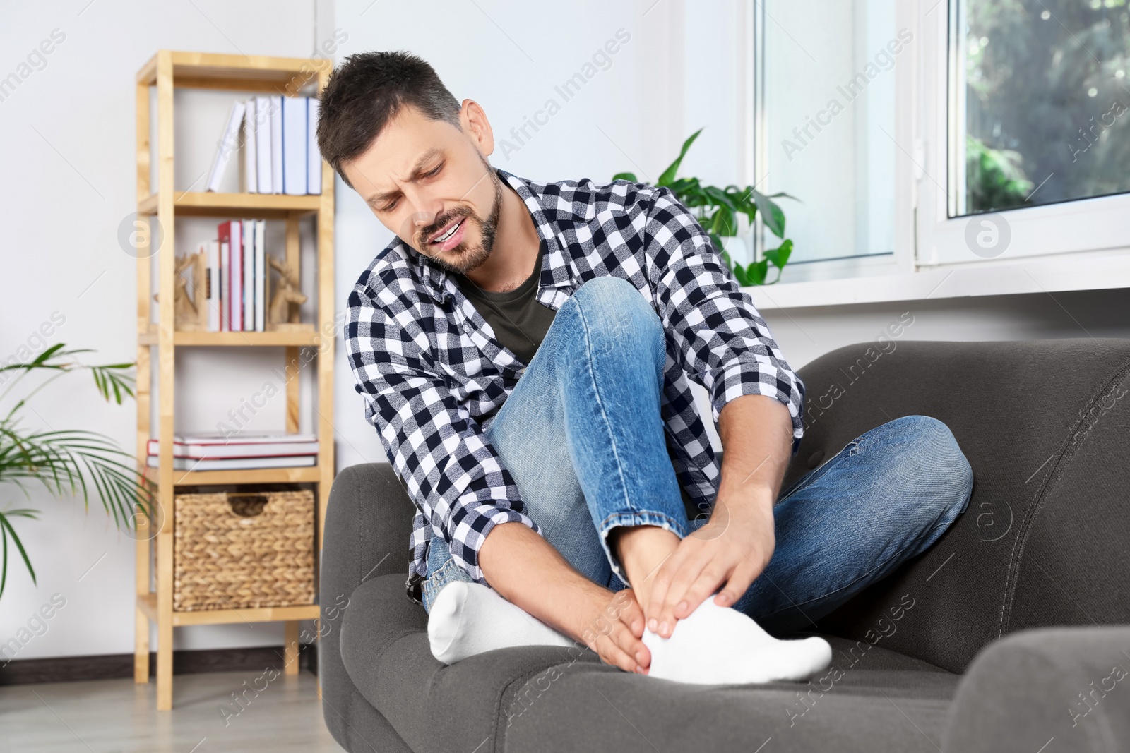 Photo of Man suffering from pain in leg on sofa at home