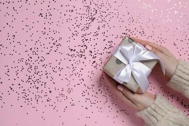 Christmas present. Woman holding gift box and confetti on pink background, top view. Space for text