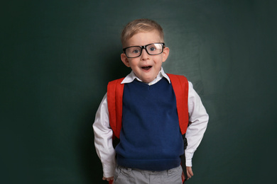 Photo of Funny little child wearing glasses near chalkboard. First time at school