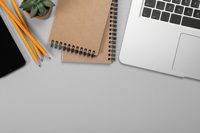 Photo of Modern laptop, stationery, smartphone and houseplant on light grey table, flat lay. Space for text