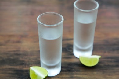 Mexican tequila shots with lime slices on wooden table, closeup. Drink made from agave
