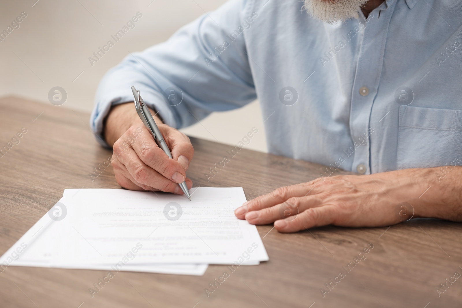 Photo of Senior man signing Last Will and Testament at wooden table, closeup