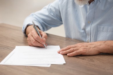Senior man signing Last Will and Testament at wooden table, closeup