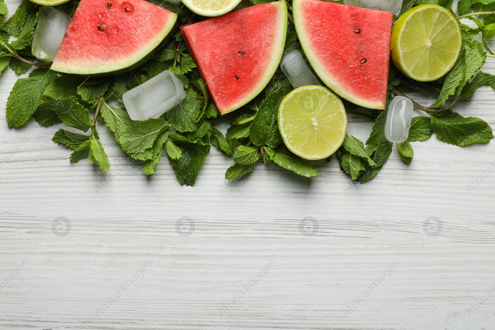 Photo of Tasty sliced watermelon, limes, mint and ice on white wooden table, flat lay. Space for text