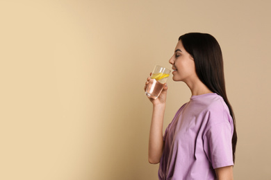 Beautiful young woman drinking tasty lemon water on beige background. Space for text