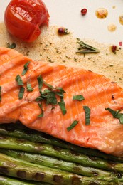 Photo of Tasty grilled salmon with tomato, asparagus and spices on plate, top view