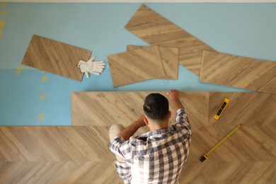 Photo of Professional worker installing new parquet flooring indoors, top view
