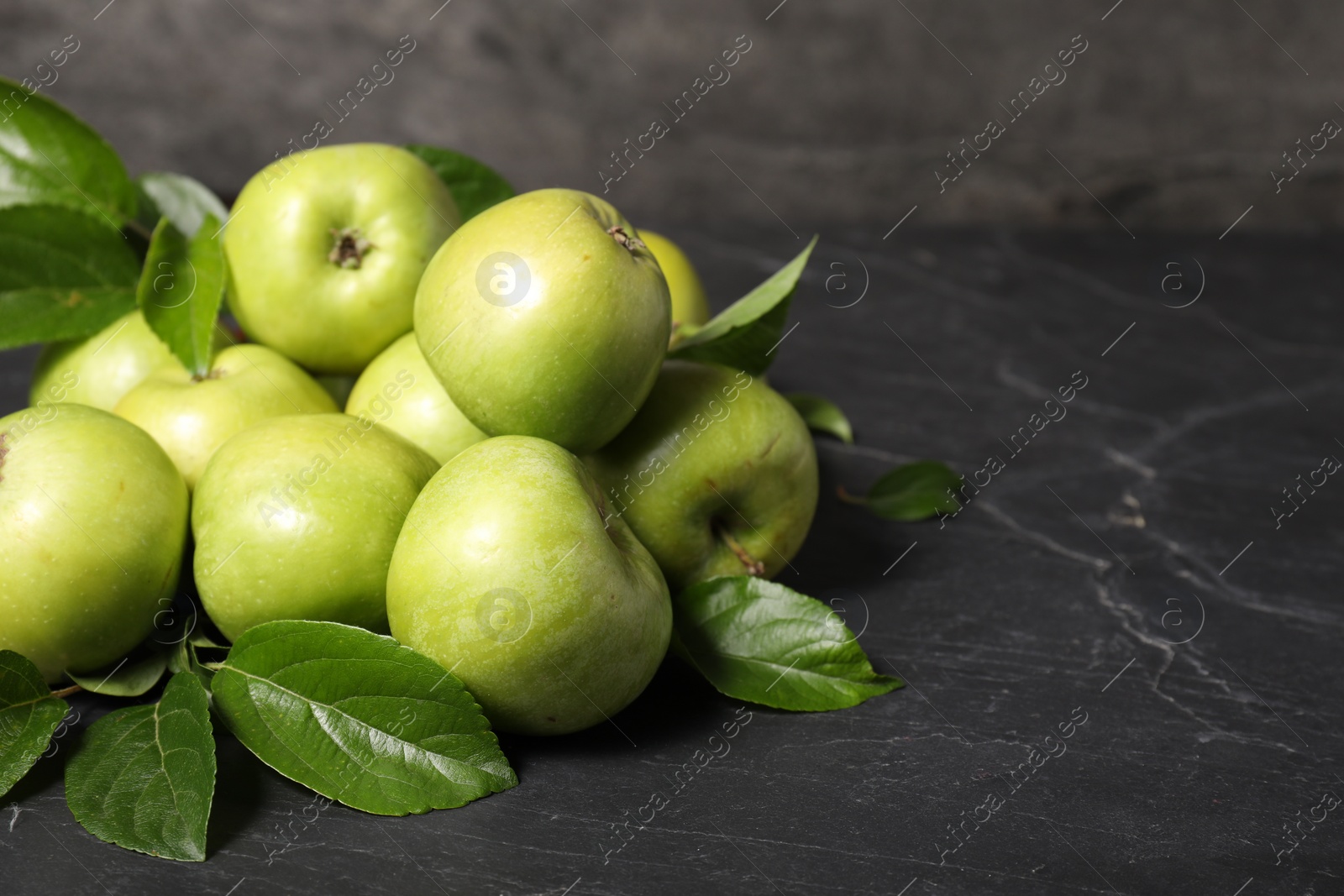 Photo of Ripe green apples with leaves on dark grey table. Space for text