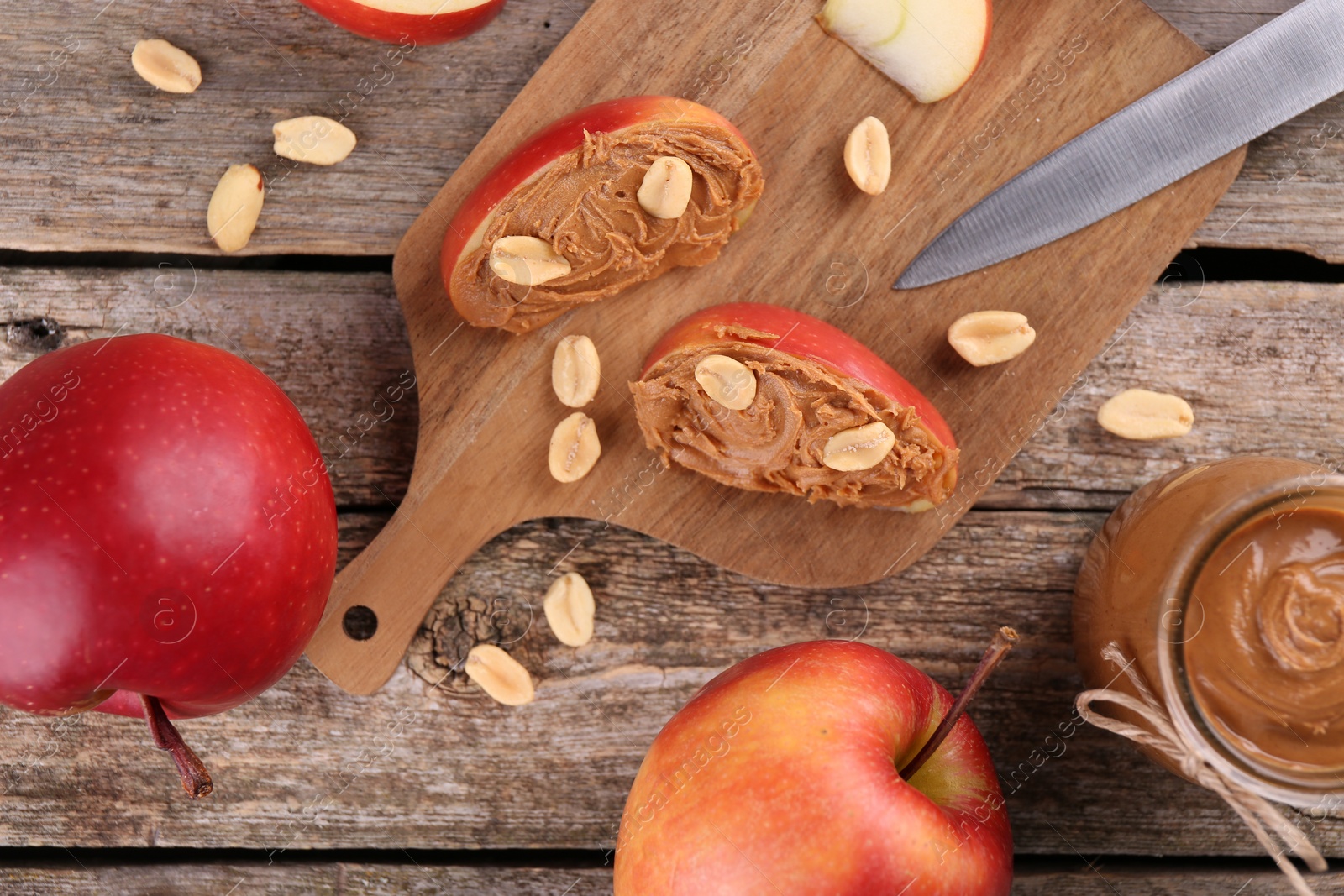 Photo of Fresh apples with peanut butter and knife on wooden table, flat lay