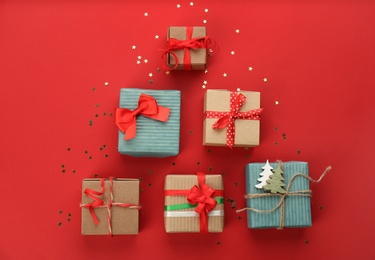 Photo of Christmas tree shape of gift boxes on red background, flat lay. Space for text