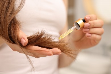 Photo of Woman applying oil hair mask indoors, closeup