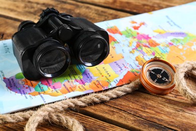 Modern binoculars, map, compass and rope on wooden table