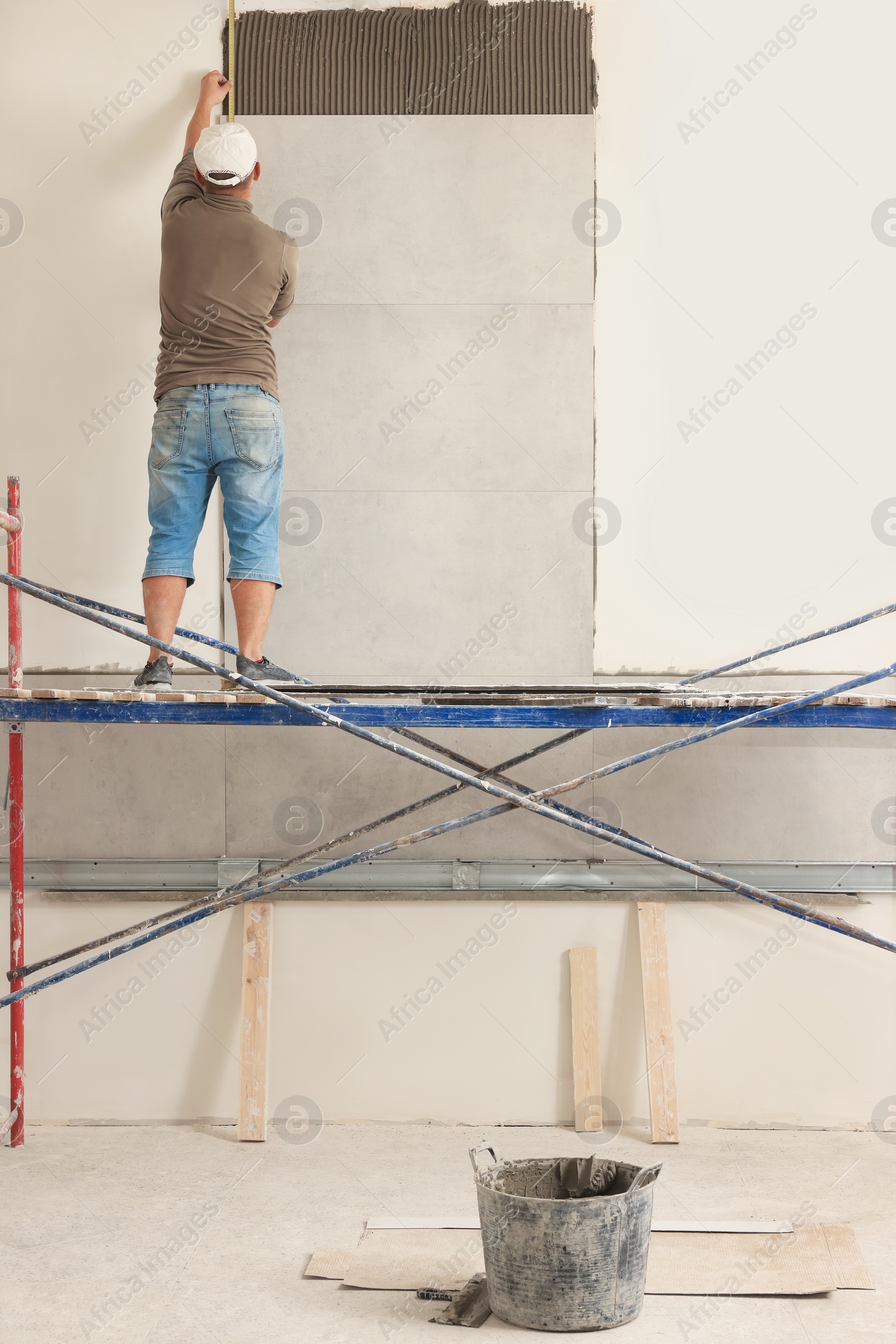 Photo of Worker installing tile on wall indoors, back view