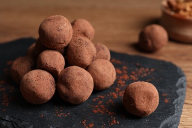 Photo of Tasty chocolate truffles powdered with cacao on slate board, closeup