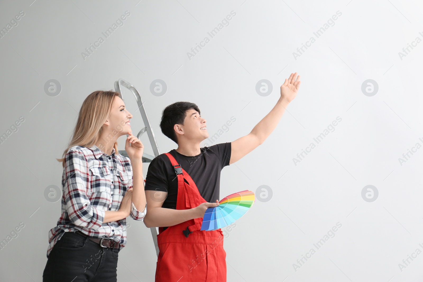 Photo of Male decorator and young woman choosing color for walls in empty room