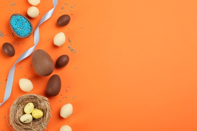 Photo of Flat lay composition with sweet chocolate eggs on orange background. Space for text