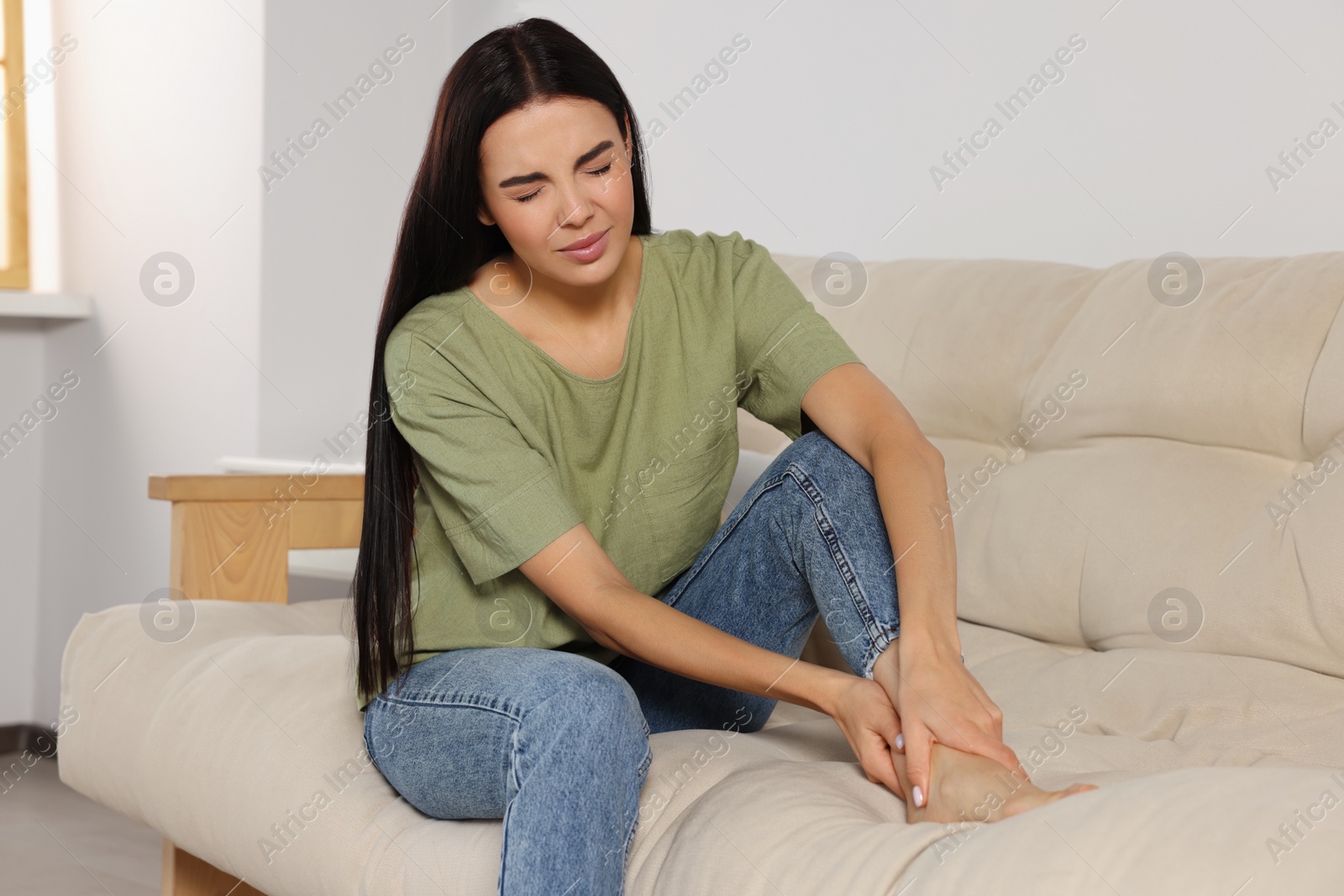 Photo of Woman rubbing sore leg on sofa at home