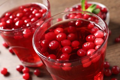 Photo of Tasty cranberry juice in glasses and fresh berries on wooden table, closeup