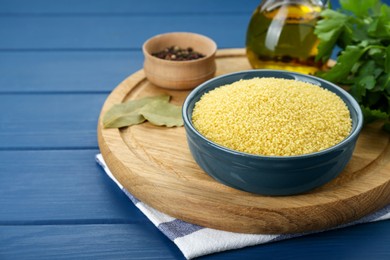 Photo of Bowl of raw couscous and ingredients on blue wooden table. Space for text