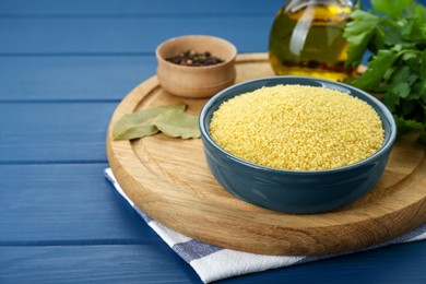 Bowl of raw couscous and ingredients on blue wooden table. Space for text