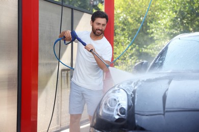 Happy man washing auto with high pressure water jet at outdoor car wash
