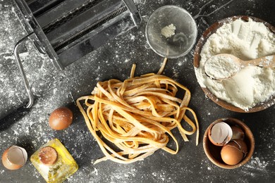 Homemade pasta, maker and ingredients on dark grey table, flat lay