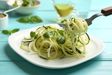 Photo of Eating delicious zucchini pasta with basil on light blue wooden table, closeup