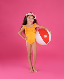 Photo of Cute little child in beachwear with bright inflatable ball on pink background