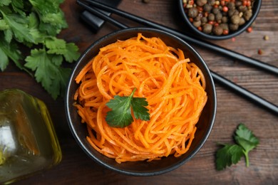 Photo of Delicious Korean carrot salad, oil, spices and parsley on wooden table, flat lay